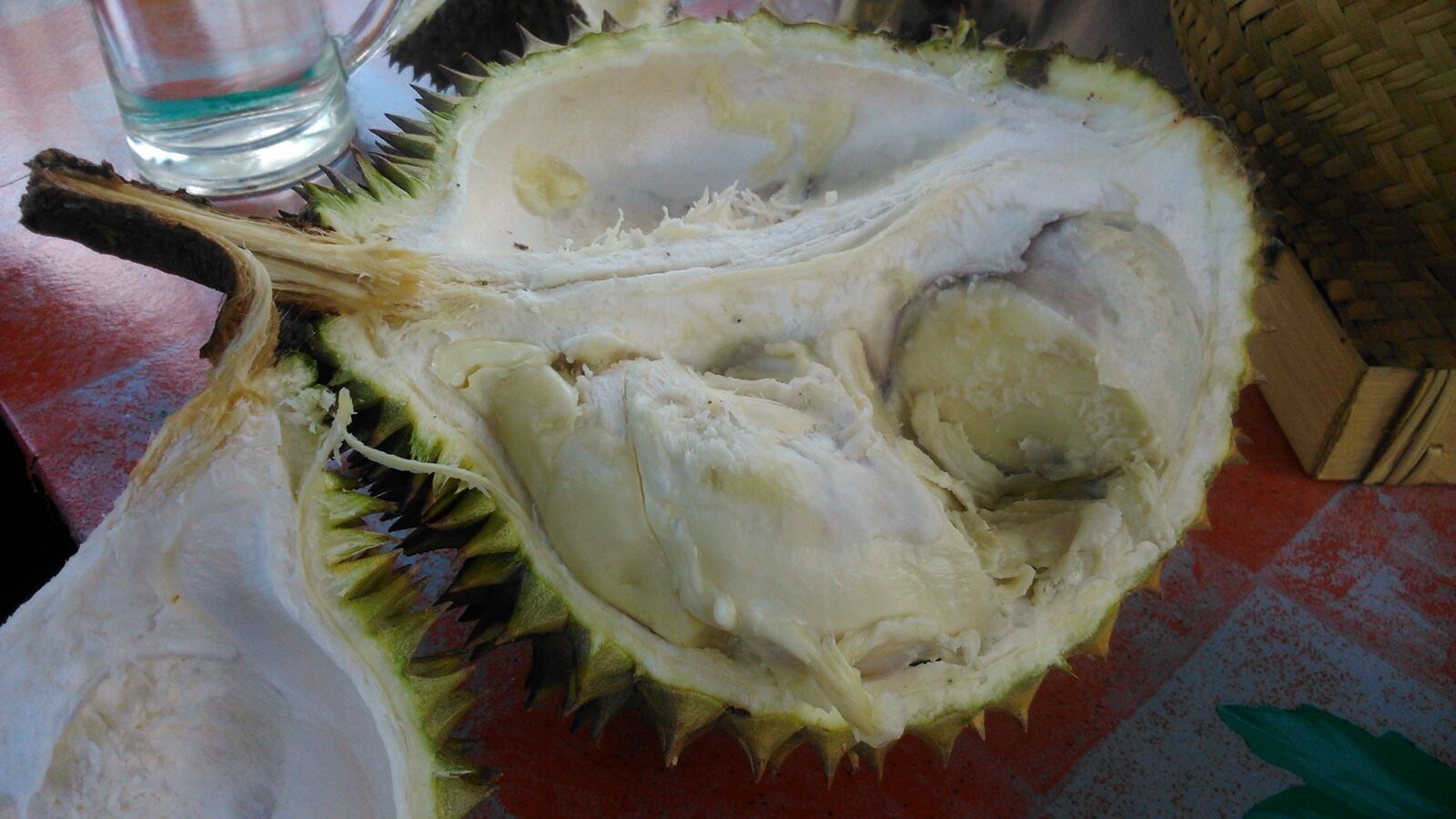 A spiky green durian fruit split open to show the pale custard-like flesh