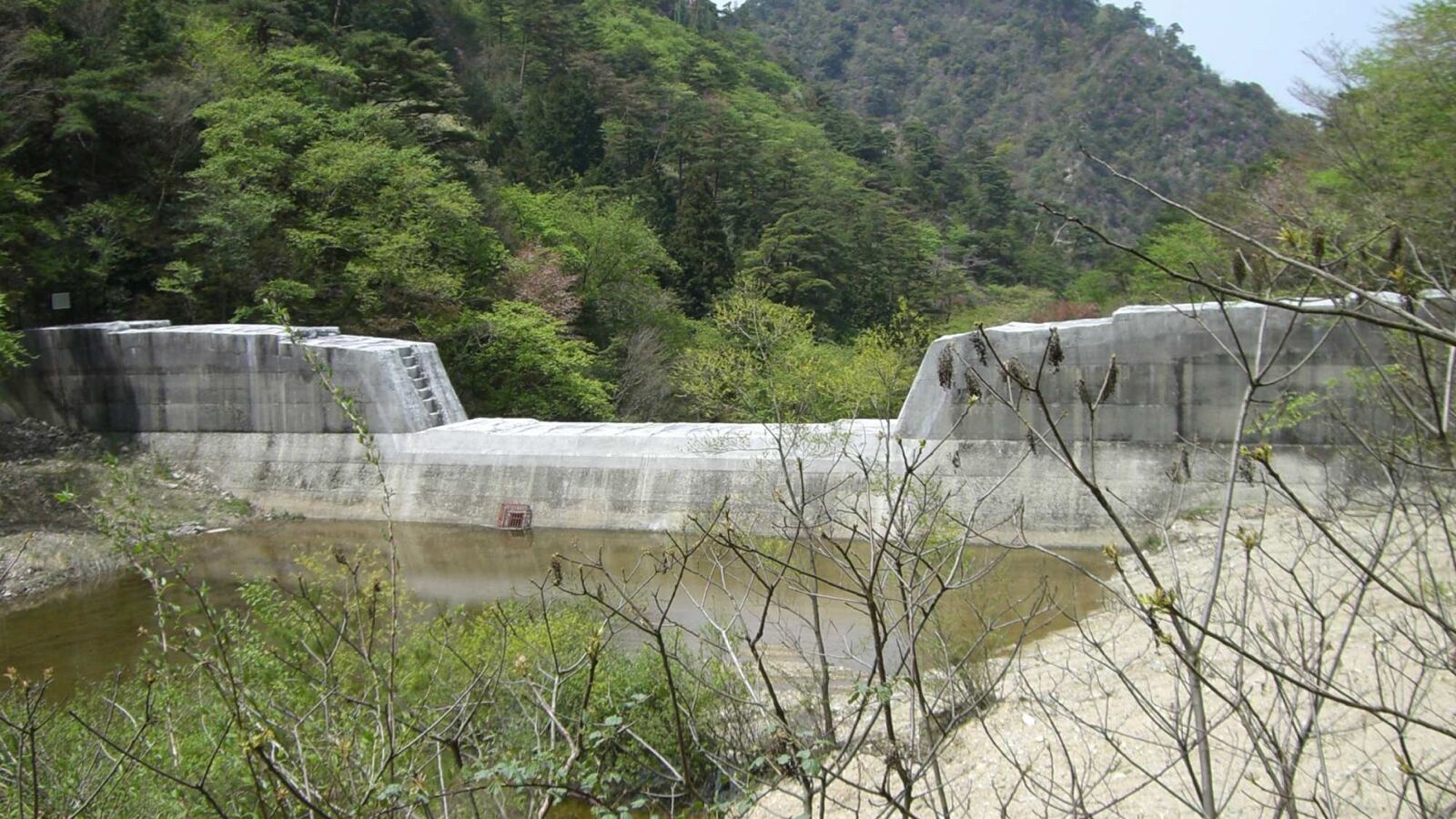 A low concrete wall across a dry sandy riverbed, with sand piled deep behind it