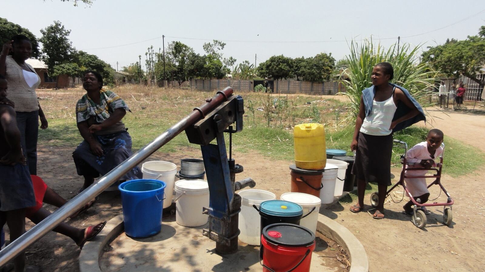 A borehole wellhead with pump housing beside a traditional stone-lined dug well